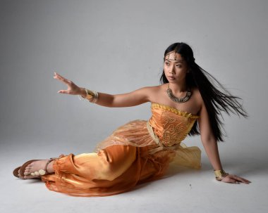 Altın Arap cübbesi giyen, stüdyo arka planında izole bir şekilde oturan, cin gibi uzun boylu Asyalı bir kadının portresi..