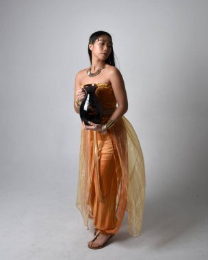 Altın Arap cübbesi giyen, elinde vazo tutan, stüdyo arka planında izole bir vazo tutan Asyalı güzel bir kadının tam boy portresi..