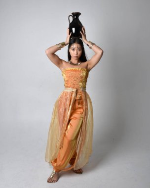 Altın Arap cübbesi giyen, elinde vazo tutan, stüdyo arka planında izole bir vazo tutan Asyalı güzel bir kadının tam boy portresi..