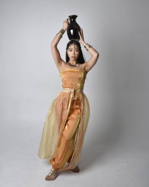 Altın Arap cübbesi giyen, elinde vazo tutan, stüdyo arka planında izole bir vazo tutan Asyalı güzel bir kadının tam boy portresi..