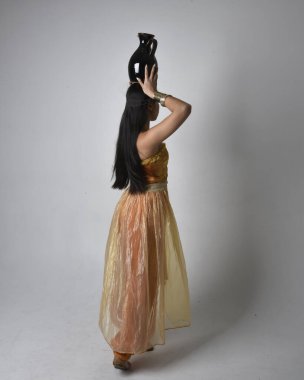 Altın Arap cübbesi giyen, elinde vazo tutan, stüdyo arka planında izole bir vazo tutan Asyalı güzel bir kadının tam boy portresi..