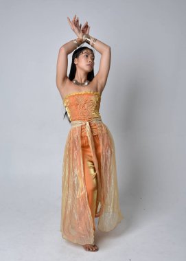 Altın Arap cübbesi giymiş güzel Asyalı bir kadının tam boy portresi. Stüdyo arka planında izole bir şekilde kameraya dönük poz veriyor..