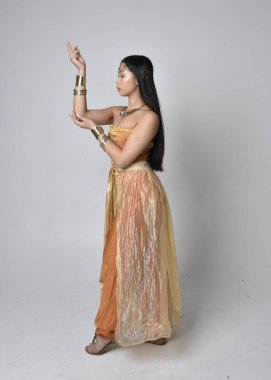 Altın Arap cübbesi giymiş güzel Asyalı bir kadının tam boy portresi. Stüdyo arka planında izole bir şekilde kameraya dönük poz veriyor..