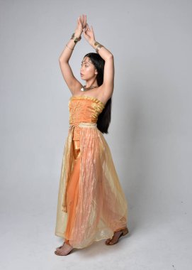 Altın Arap cübbesi giymiş güzel Asyalı bir kadının tam boy portresi. Stüdyo arka planında izole bir şekilde kameraya dönük poz veriyor..