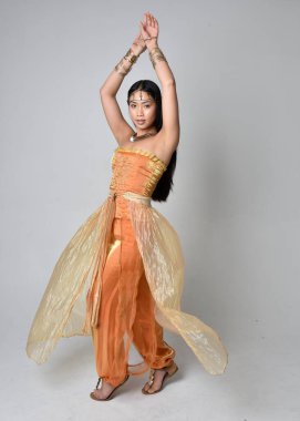 Altın Arap cübbesi giymiş güzel Asyalı bir kadının tam boy portresi. Stüdyo arka planında izole bir şekilde kameraya dönük poz veriyor..