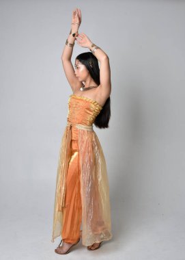 Altın Arap cübbesi giymiş güzel Asyalı bir kadının tam boy portresi. Stüdyo arka planında izole bir şekilde kameraya dönük poz veriyor..