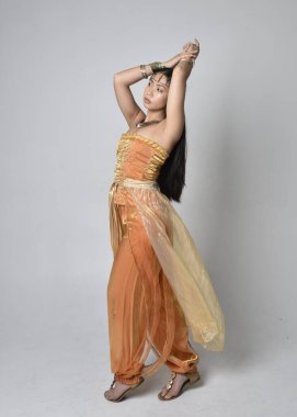 Altın Arap cübbesi giymiş güzel Asyalı bir kadının tam boy portresi. Stüdyo arka planında izole bir şekilde kameraya dönük poz veriyor..