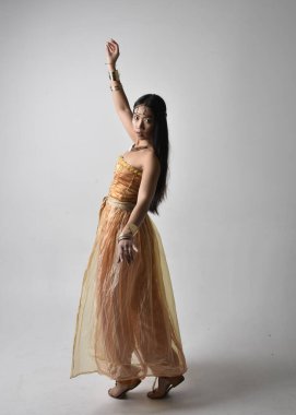 Altın Arap cübbesi giymiş güzel Asyalı bir kadının tam boy portresi. Stüdyo arka planında izole bir şekilde kameraya dönük poz veriyor..