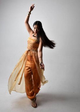 Altın Arap cübbesi giymiş güzel Asyalı bir kadının tam boy portresi. Stüdyo arka planında izole bir şekilde kameraya dönük poz veriyor..