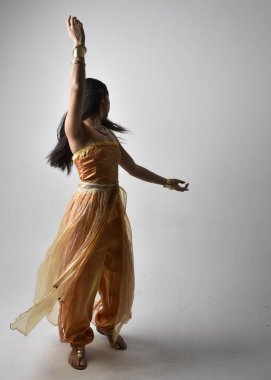 Altın Arap cübbesi giymiş güzel Asyalı bir kadının tam boy portresi. Stüdyo arka planında izole bir şekilde kameraya dönük poz veriyor..