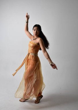 Altın Arap cübbesi giymiş güzel Asyalı bir kadının tam boy portresi. Stüdyo arka planında izole bir şekilde kameraya dönük poz veriyor..