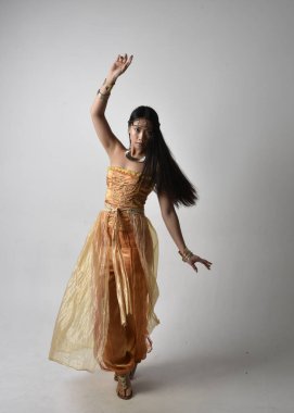 Altın Arap cübbesi giymiş güzel Asyalı bir kadının tam boy portresi. Stüdyo arka planında izole bir şekilde kameraya dönük poz veriyor..