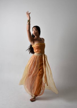 Altın Arap cübbesi giymiş güzel Asyalı bir kadının tam boy portresi. Stüdyo arka planında izole bir şekilde kameraya dönük poz veriyor..