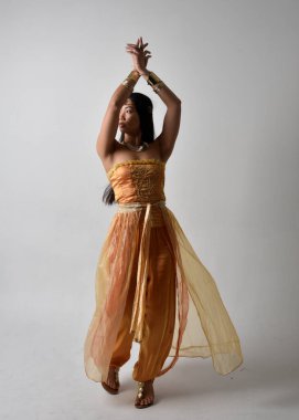 Altın Arap cübbesi giymiş güzel Asyalı bir kadının tam boy portresi. Stüdyo arka planında izole bir şekilde kameraya dönük poz veriyor..