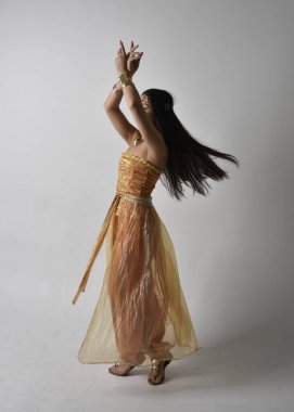 Altın Arap cübbesi giymiş güzel Asyalı bir kadının tam boy portresi. Stüdyo arka planında izole bir şekilde kameraya dönük poz veriyor..