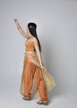 Altın Arap cübbesi giymiş güzel Asyalı bir kadının tam boy portresi. Stüdyo arka planında izole bir şekilde kameraya dönük poz veriyor..