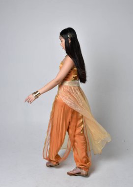 Altın Arap cübbesi giymiş güzel Asyalı bir kadının tam boy portresi. Stüdyo arka planında izole bir şekilde kameraya dönük poz veriyor..