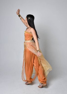 Altın Arap cübbesi giymiş güzel Asyalı bir kadının tam boy portresi. Stüdyo arka planında izole bir şekilde kameraya dönük poz veriyor..