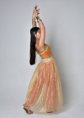 Altın Arap cübbesi giymiş güzel Asyalı bir kadının tam boy portresi. Stüdyo arka planında izole bir şekilde kameraya dönük poz veriyor..