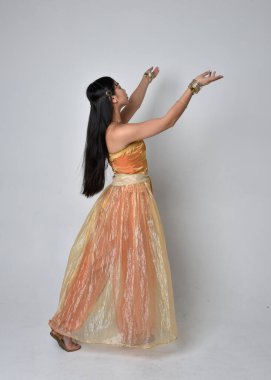 Altın Arap cübbesi giymiş güzel Asyalı bir kadının tam boy portresi. Stüdyo arka planında izole bir şekilde kameraya dönük poz veriyor..