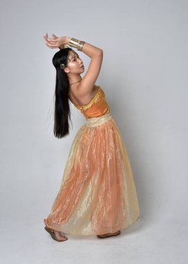 Altın Arap cübbesi giymiş güzel Asyalı bir kadının tam boy portresi. Stüdyo arka planında izole bir şekilde kameraya dönük poz veriyor..