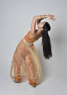 Altın Arap cübbesi giymiş güzel Asyalı bir kadının tam boy portresi. Stüdyo arka planında izole bir şekilde kameraya dönük poz veriyor..