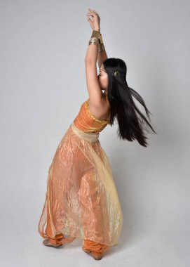 Altın Arap cübbesi giymiş güzel Asyalı bir kadının tam boy portresi. Stüdyo arka planında izole bir şekilde kameraya dönük poz veriyor..