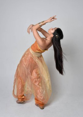 Altın Arap cübbesi giymiş güzel Asyalı bir kadının tam boy portresi. Stüdyo arka planında izole bir şekilde kameraya dönük poz veriyor..