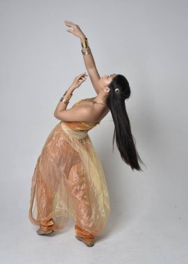 Altın Arap cübbesi giymiş güzel Asyalı bir kadının tam boy portresi. Stüdyo arka planında izole bir şekilde kameraya dönük poz veriyor..