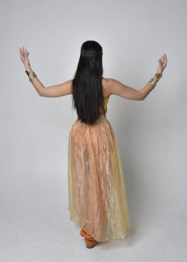 Altın Arap cübbesi giymiş güzel Asyalı bir kadının tam boy portresi. Stüdyo arka planında izole bir şekilde kameraya dönük poz veriyor..