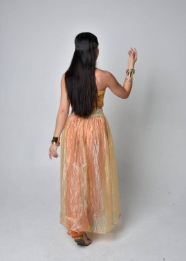 Altın Arap cübbesi giymiş güzel Asyalı bir kadının tam boy portresi. Stüdyo arka planında izole bir şekilde kameraya dönük poz veriyor..