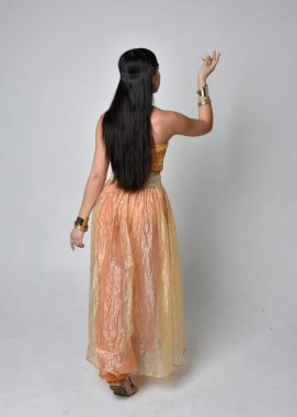 Altın Arap cübbesi giymiş güzel Asyalı bir kadının tam boy portresi. Stüdyo arka planında izole bir şekilde kameraya dönük poz veriyor..