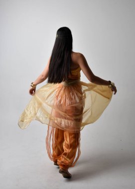 Altın Arap cübbesi giymiş güzel Asyalı bir kadının tam boy portresi. Stüdyo arka planında izole bir şekilde kameraya dönük poz veriyor..