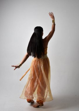 Altın Arap cübbesi giymiş güzel Asyalı bir kadının tam boy portresi. Stüdyo arka planında izole bir şekilde kameraya dönük poz veriyor..