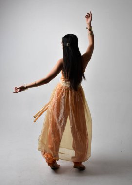 Altın Arap cübbesi giymiş güzel Asyalı bir kadının tam boy portresi. Stüdyo arka planında izole bir şekilde kameraya dönük poz veriyor..