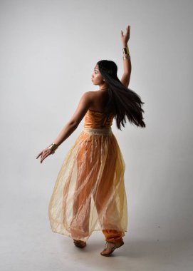 Altın Arap cübbesi giymiş güzel Asyalı bir kadının tam boy portresi. Stüdyo arka planında izole bir şekilde kameraya dönük poz veriyor..