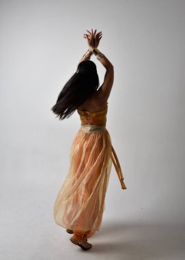 Altın Arap cübbesi giymiş güzel Asyalı bir kadının tam boy portresi. Stüdyo arka planında izole bir şekilde kameraya dönük poz veriyor..