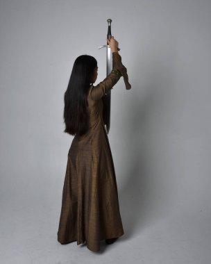 Orta çağ fantezi elbisesi giymiş uzun saçlı güzel Asyalı bir kadının tam boy portresi. Kılıç tutan zarif duruş, stüdyo arka planında izole edilmiş..