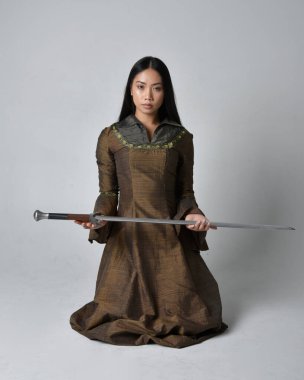 Orta çağ fantezi elbisesi giymiş uzun saçlı güzel Asyalı bir kadının tam boy portresi. Kılıç tutan zarif bir poz, stüdyo arka planında izole edilmiş..