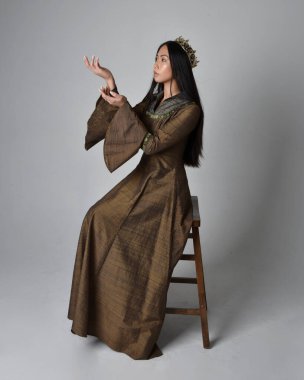 Orta çağ fantezi elbisesi ve altın kaplama kostüm giyen uzun saçlı güzel Asyalı kadının tam boy portresi. Zarif bir poz, stüdyo arka planında izole..