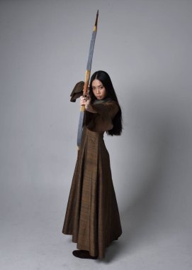 Orta çağ fantezi elbisesi giymiş, uzun saçlı güzel Asyalı bir kadının portresi. Uzun bir yay ve ok tutan zarif bir poz, stüdyo arka planında izole edilmiş..