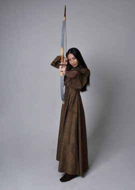 Orta çağ fantezi elbisesi giymiş, uzun saçlı güzel Asyalı bir kadının portresi. Uzun bir yay ve ok tutan zarif bir poz, stüdyo arka planında izole edilmiş..