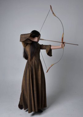 Orta çağ fantezi elbisesi giymiş, uzun saçlı güzel Asyalı bir kadının portresi. Uzun bir yay ve ok tutan zarif bir poz, stüdyo arka planında izole edilmiş..