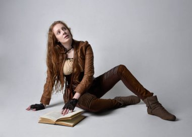 Uzun kızıl saçlı, Steampunk 'tan esinlenilmiş bir kostüm giymiş güzel bir genç kadının tam boy portresi. Stüdyo arka planında izole edilmiş poz.