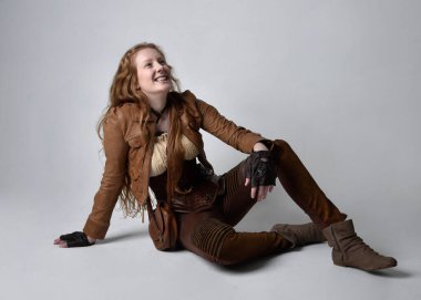 Uzun kızıl saçlı, Steampunk 'tan esinlenilmiş bir kostüm giymiş güzel bir genç kadının tam boy portresi. Stüdyo arka planında izole edilmiş poz.