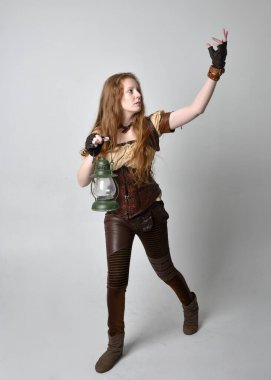 Uzun kızıl saçlı, Steampunk 'tan esinlenilmiş bir kostüm giymiş stüdyo arka planında izole edilmiş fener tutan güzel bir genç kadın portresi..