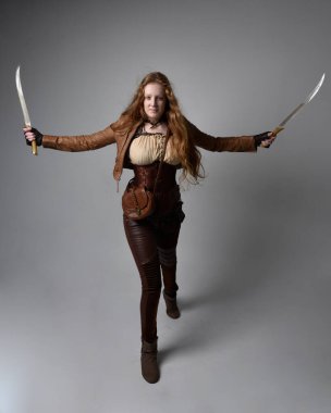 Uzun kızıl saçlı, Steampunk 'tan esinlenilmiş, stüdyo arka planında izole edilmiş bıçaklı güzel bir genç kadının portresi..