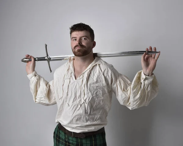 スコットランドのキルトとルネッサンスの白い海賊ブラウスシャツを着てハンサムなブルネットの男の肖像画を閉じます 武器を保持し スタジオの背景に隔離されたアクションポーズ — ストック写真
