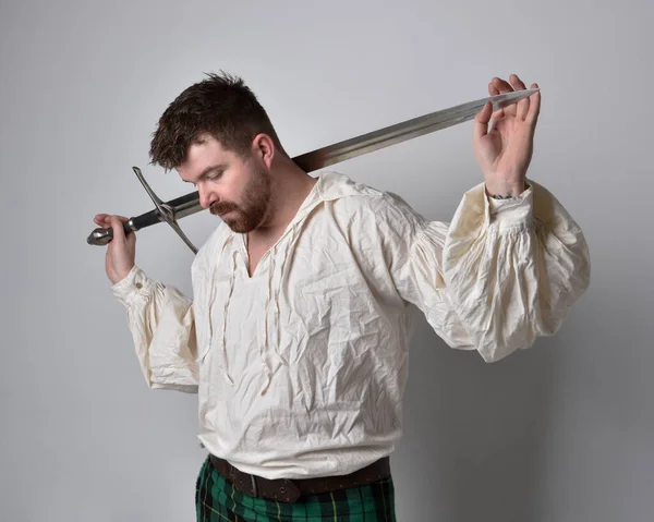 スコットランドのキルトとルネッサンスの白い海賊ブラウスシャツを着てハンサムなブルネットの男の肖像画を閉じます 武器を保持し スタジオの背景に隔離されたアクションポーズ — ストック写真