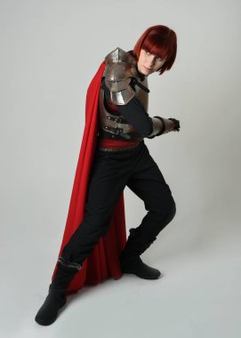 Savaşçı kadın şövalyenin tam boy fantezi portresi, tarihi ortaçağ çelik zırh kostümü giyen bir model, kırmızı peri masalı pelerini. Ayakta durma pozu, izole edilmiş stüdyo arka planı.